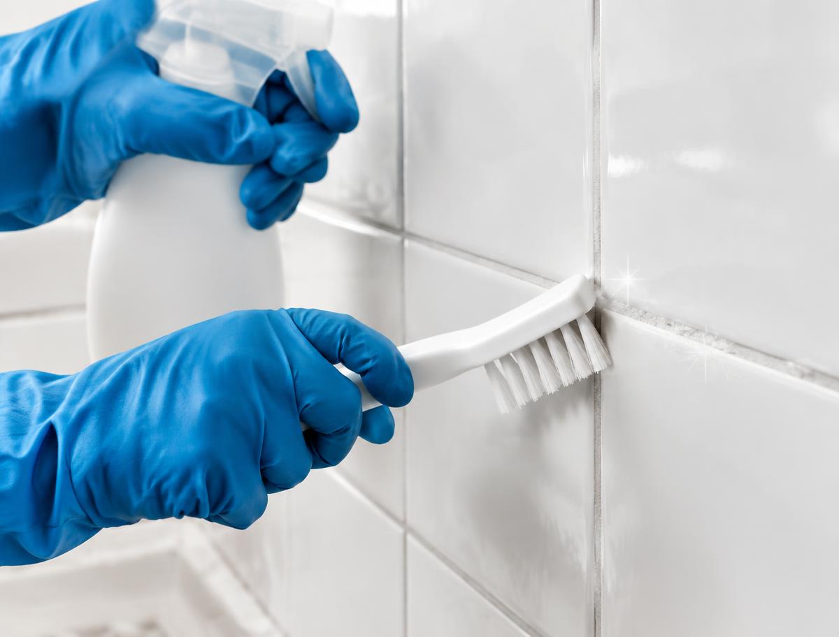 Gloved hands scrubbing white bathroom tile grout